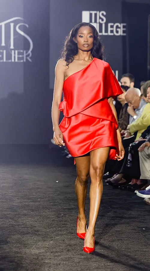 Model walking down runway wearing red dress