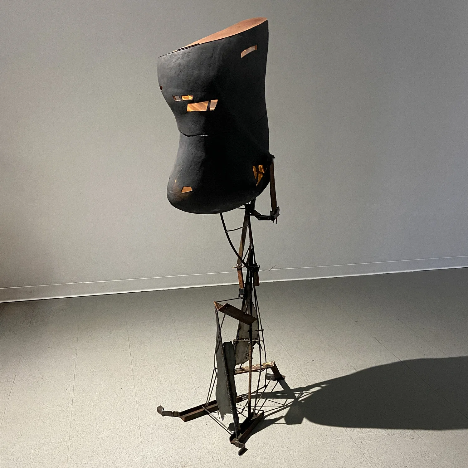 A black ceramic form, shaped like an oblong torso. Window-like cutouts in the form give way to lights on the inside, seen through a prism foil that refracts light in strange ways. It's held up by a steel frame that gives it a look of great weight.