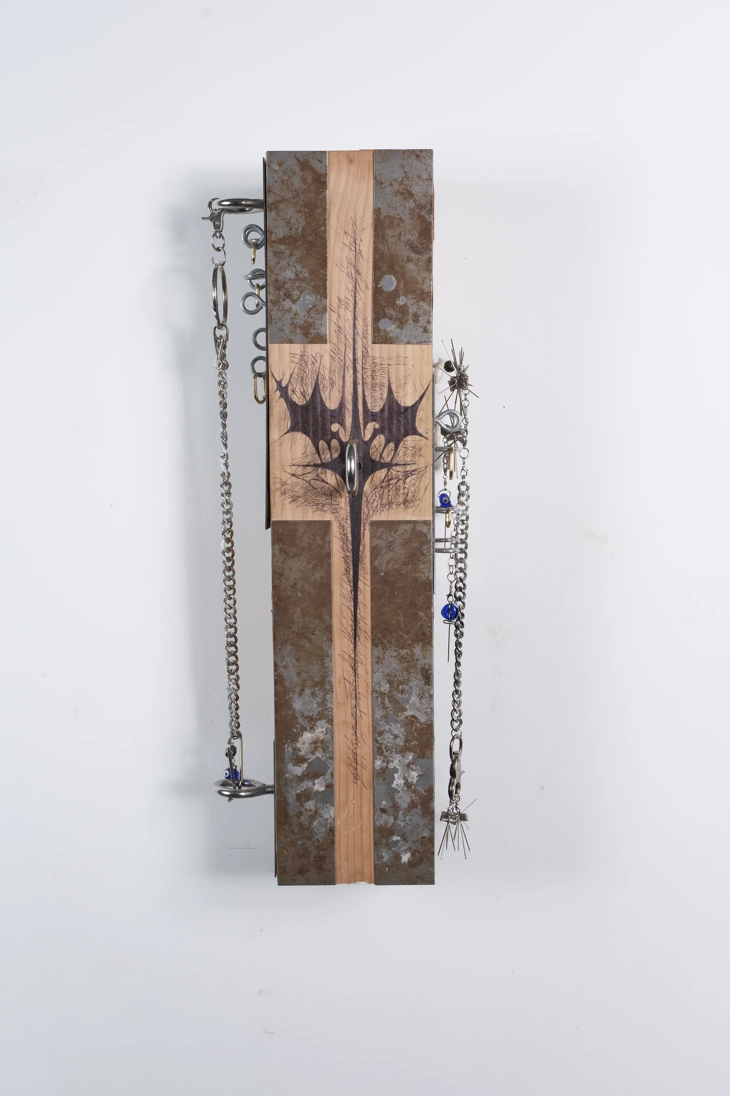 A rectangular wooden sculpture, clad with rusted metal plates, zinc screw eyes, gold hoop earrings, and other adornments made of T-Pins.