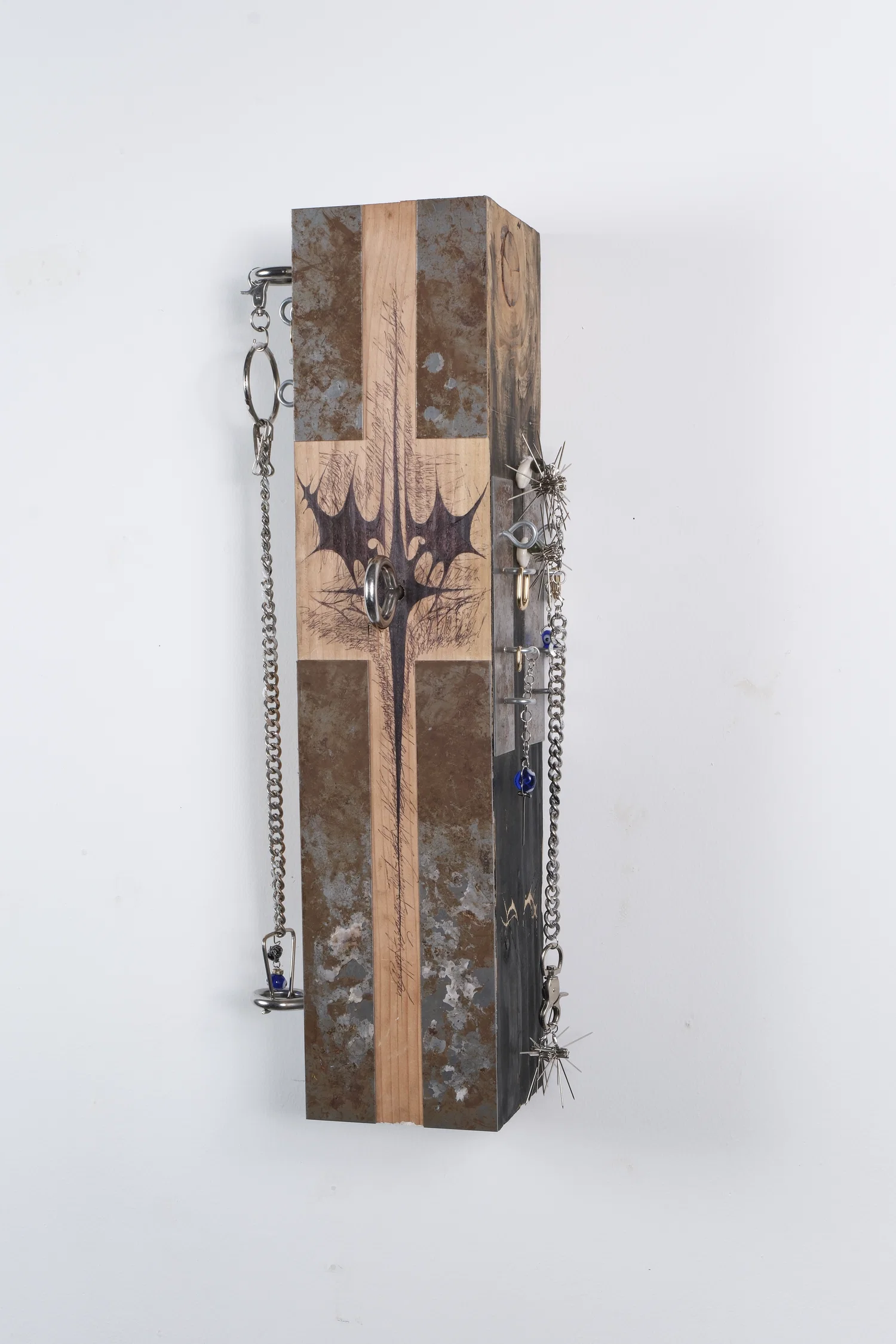 A rectangular wooden sculpture, clad with rusted metal plates, zinc screw eyes, gold hoop earrings, and other adornments made of T-Pins.
