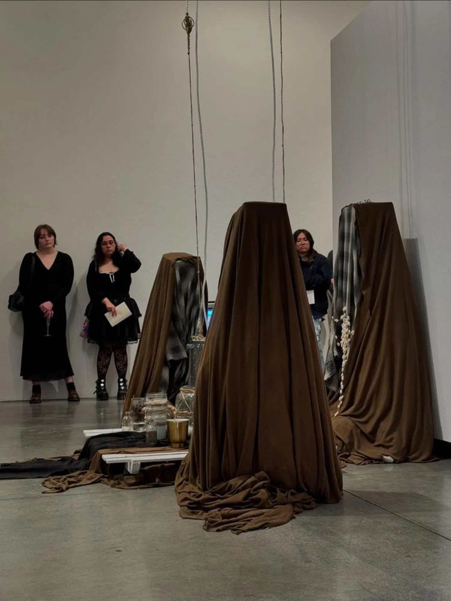 Photograph of a performance with three hooded/veiled figures performing a ritual around an altar on the floor.