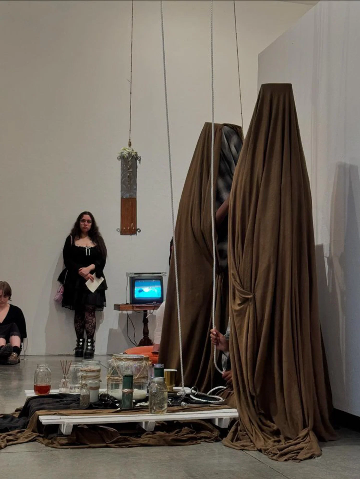 Photograph of a performance with three hooded/veiled figures performing a ritual around an altar on the floor.
