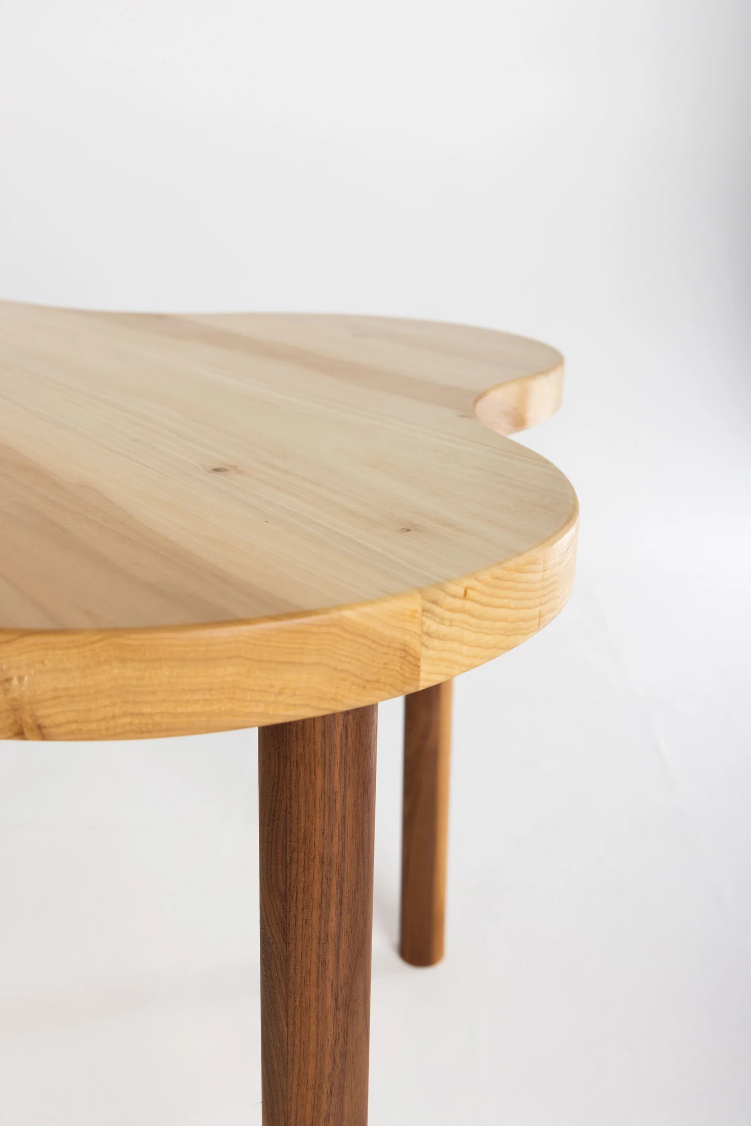 Closeup of a finely finished poplar tabletop. The tabletop has a 4-sided clover-like shape, curving in and out.