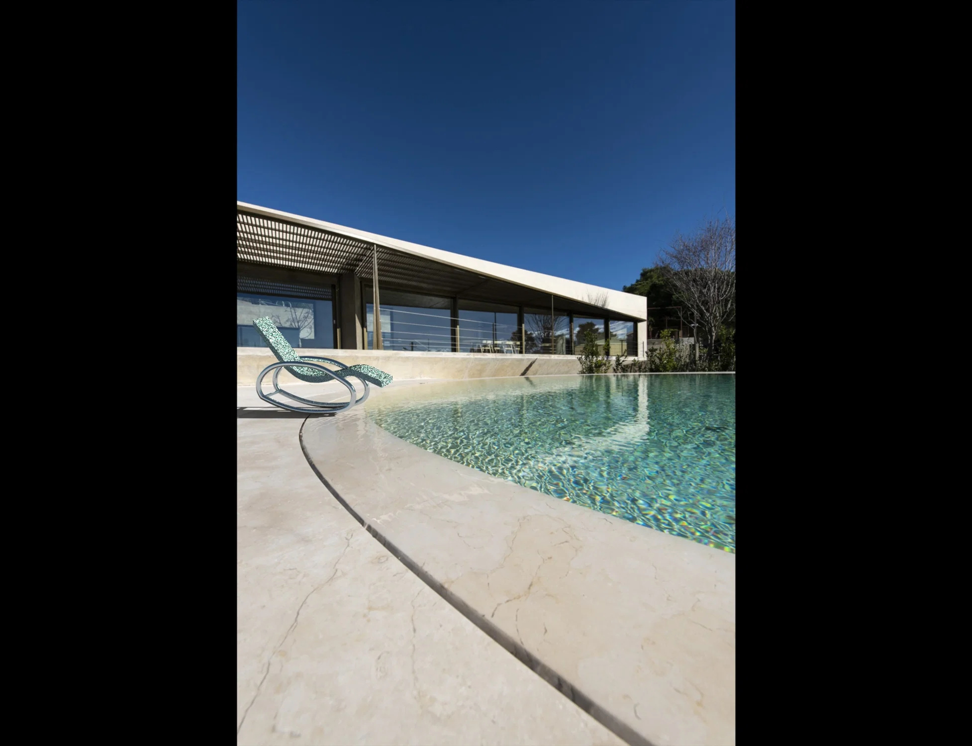 A modern lounge chair with a curved teal seat and a sleek oval metal rocking base.