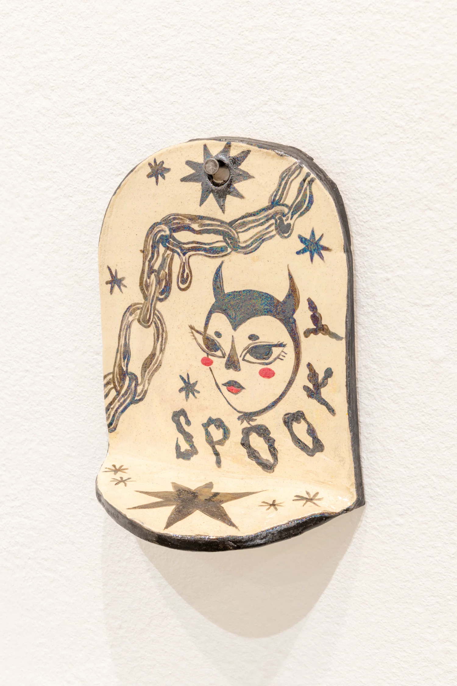 A small white ceramic wall shelf with black illustrations and the word "Spooky" on it. It has a pearlescent effect and the piece is attached to a white wall.