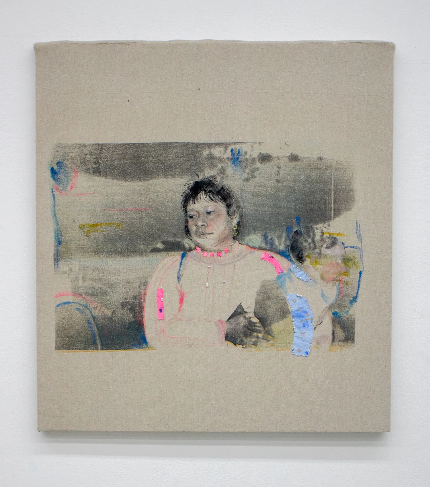 A screen printed image on top of linen. The image has transparent layers of a mother holding a child that is painted on top with acrylic paint. It is embroidered with fabric, string and beads.