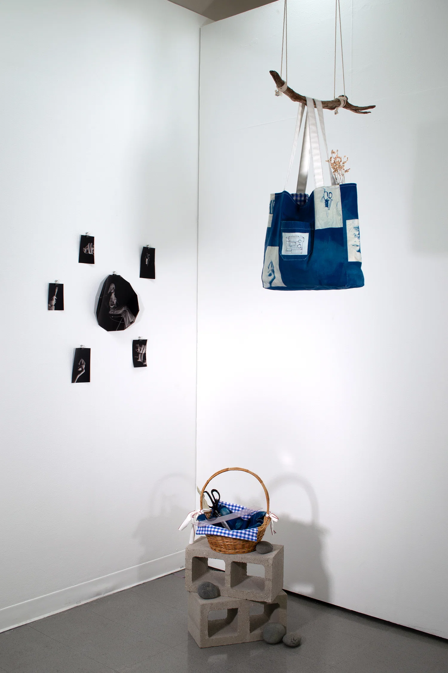 Cyanotype prints constructed into a tote bag hung on a suspended branch accompanied by a picnic basket containing the items that were photographed and used to craft the bag.