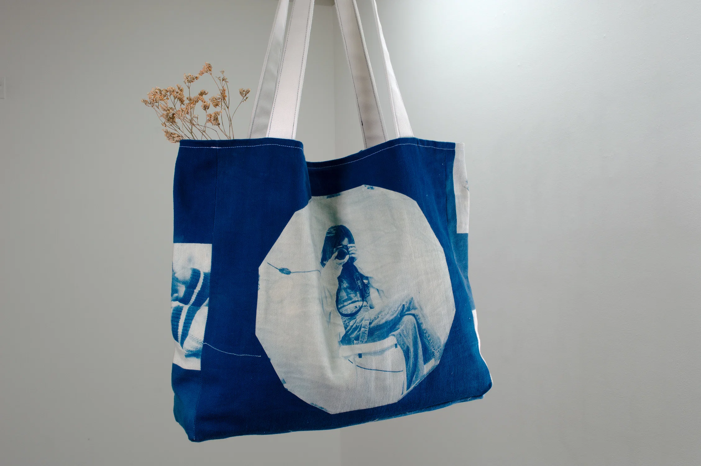A close up photo of the back of the tote bag with a cyanotype print of a self-portrait. The bag contains dried pink flowers sitting inside.