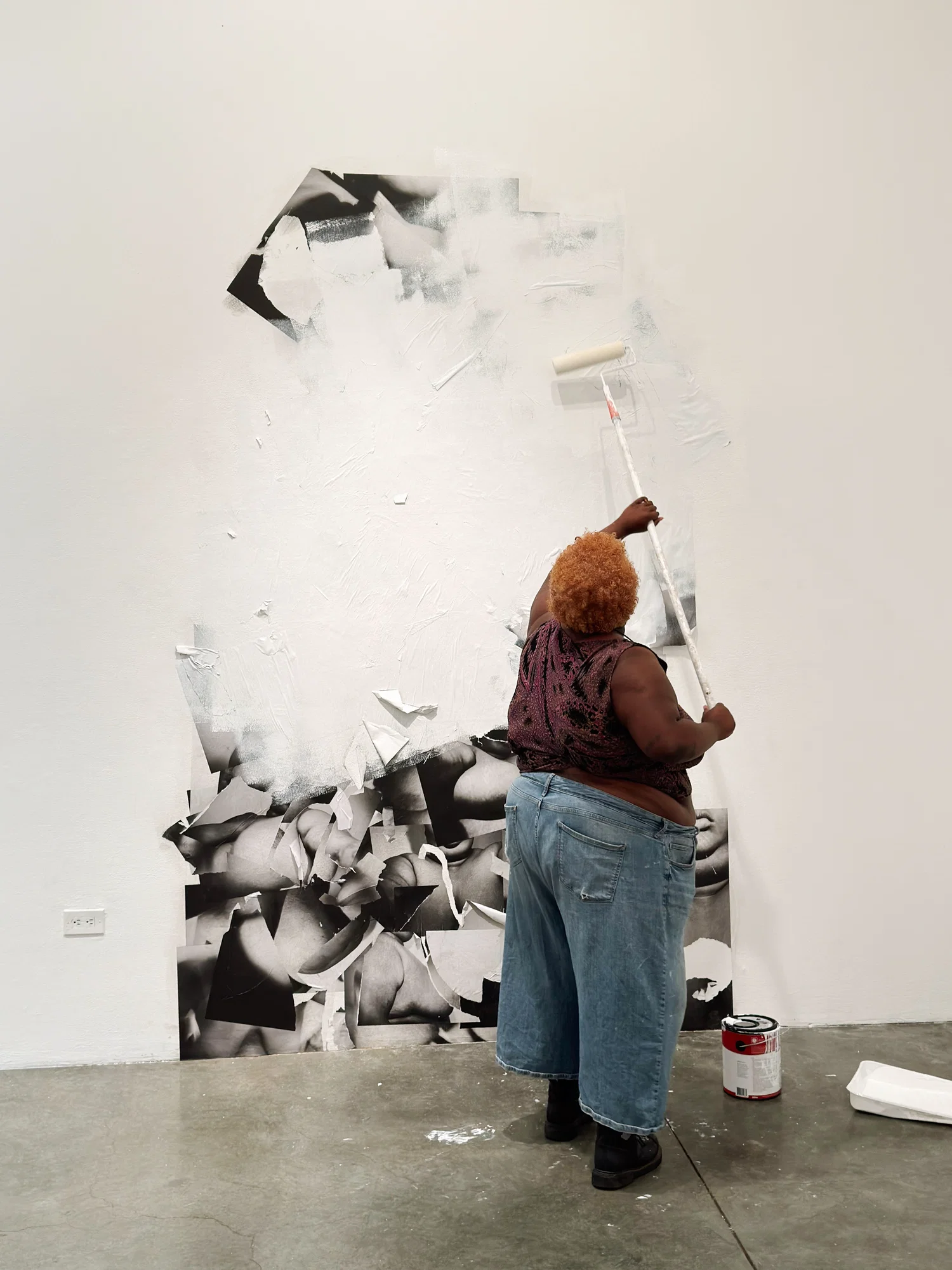 black and white prints of figure wheat pasted on the wall. same figure as seen in images, stands infront of the prints and paints over them with white paint, matching the wall.