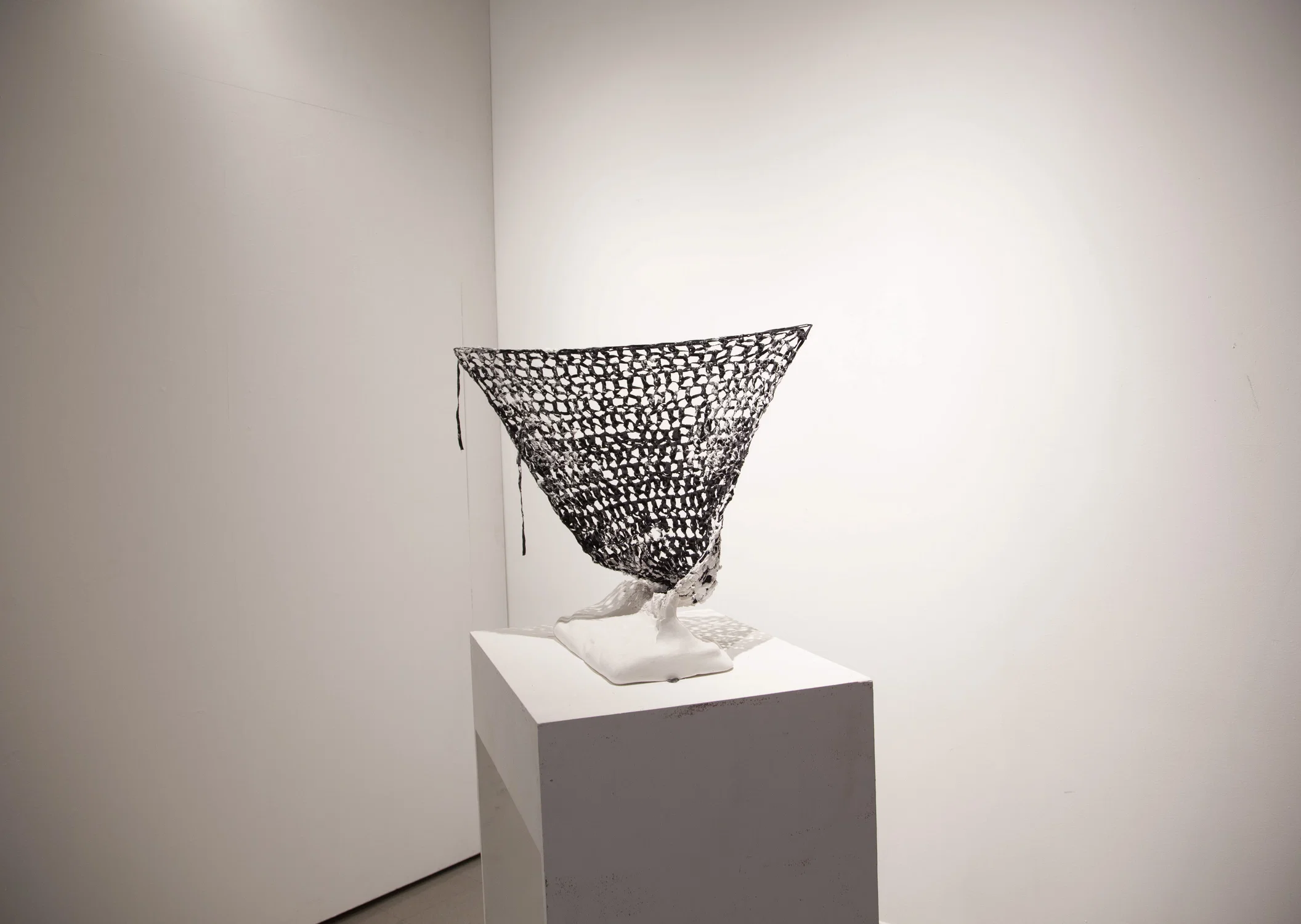 white plaster sculpted object with black crocheted bias tape coming out of it. The crocheted panel is suspended to the walls using string