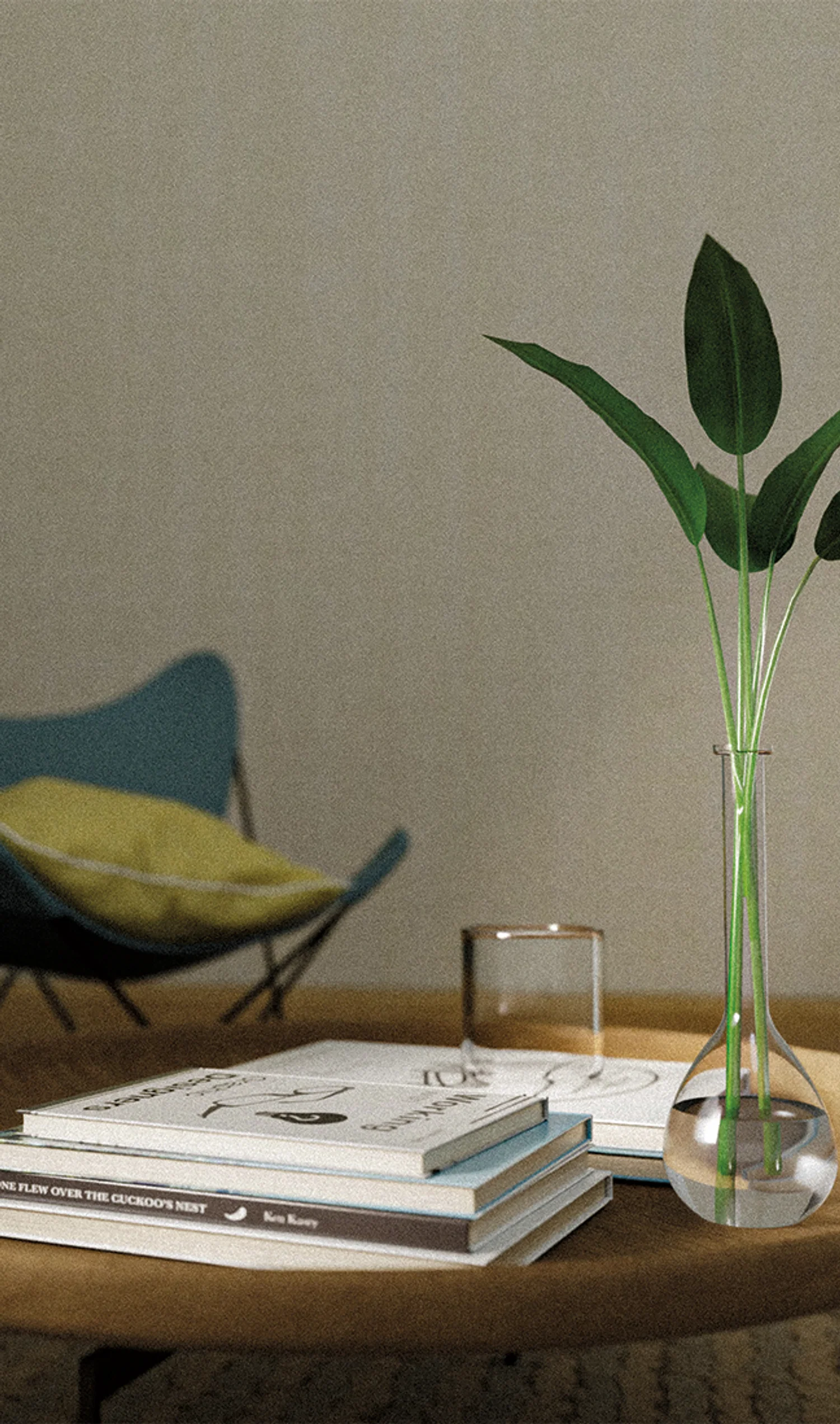 A calm indoor scene with a glass vase holding green leaves, stacked books on a wooden table, and a chair softly blurred in the background.