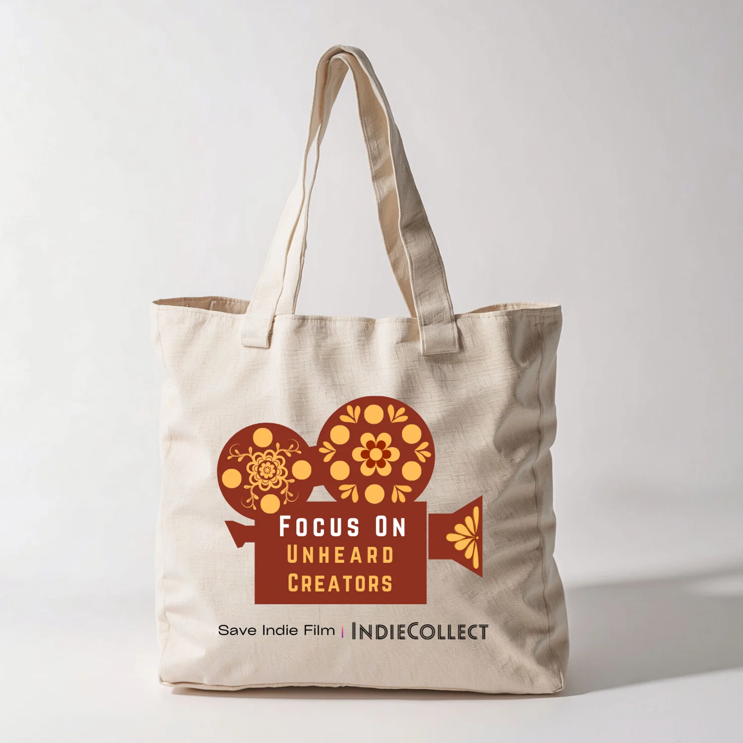 Tote bag with a vector image of a film camera with the slogan, "Focus on Unheard Creators" in the middle, with the IndieCollect logo on the bottom.