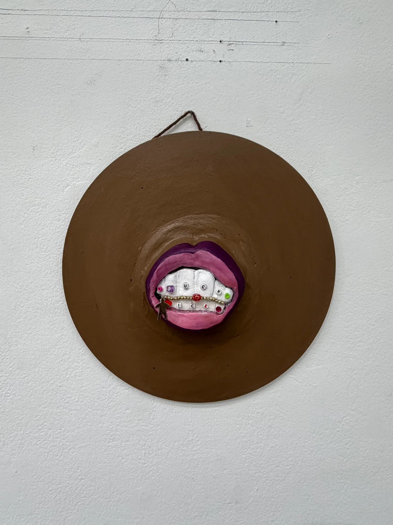 A wall mounted sculpture of a mouth with grills that spell out FUCK ICE in gems.