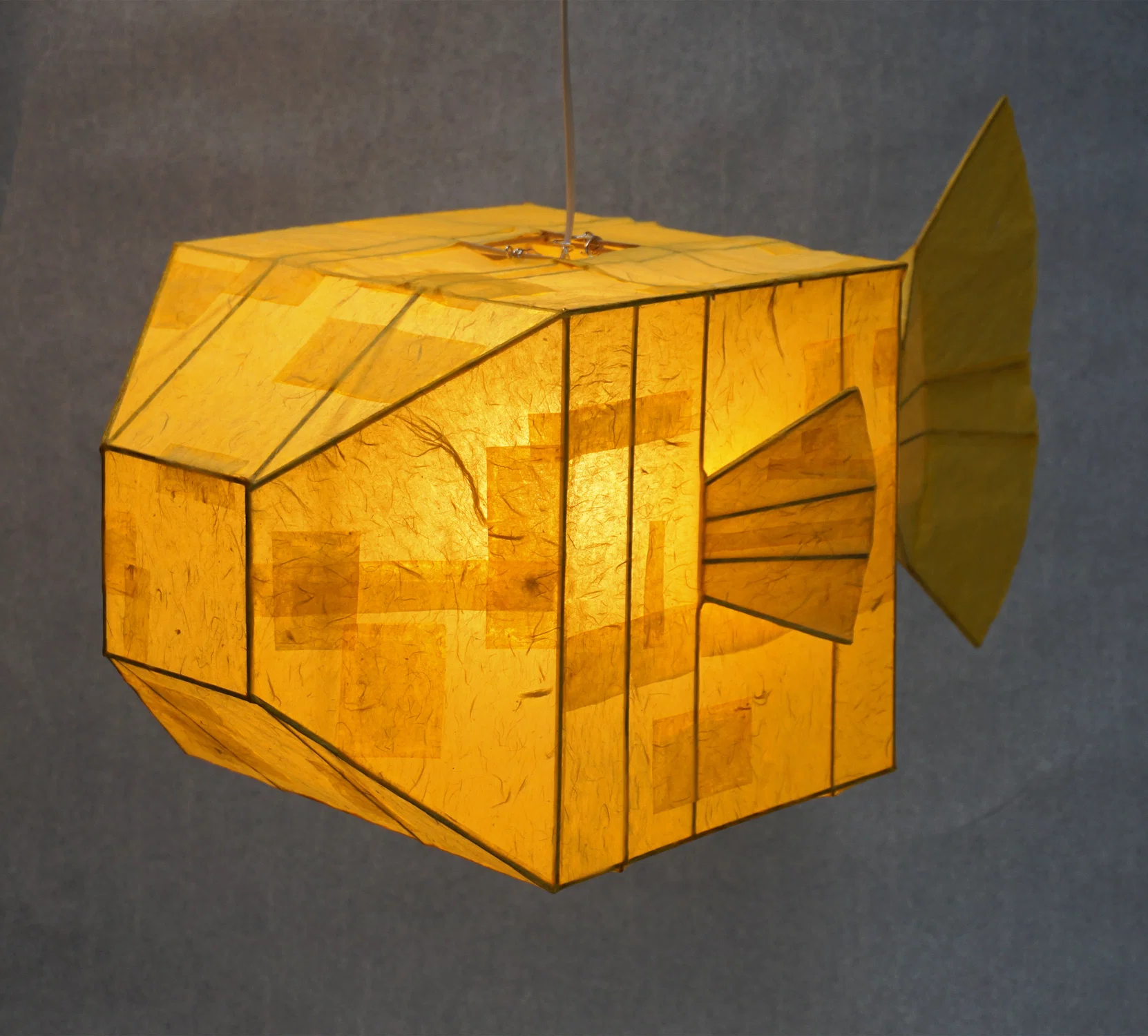 Three dimensional lamp that is a bright and warm yellow in the abstract shape of a boxfish