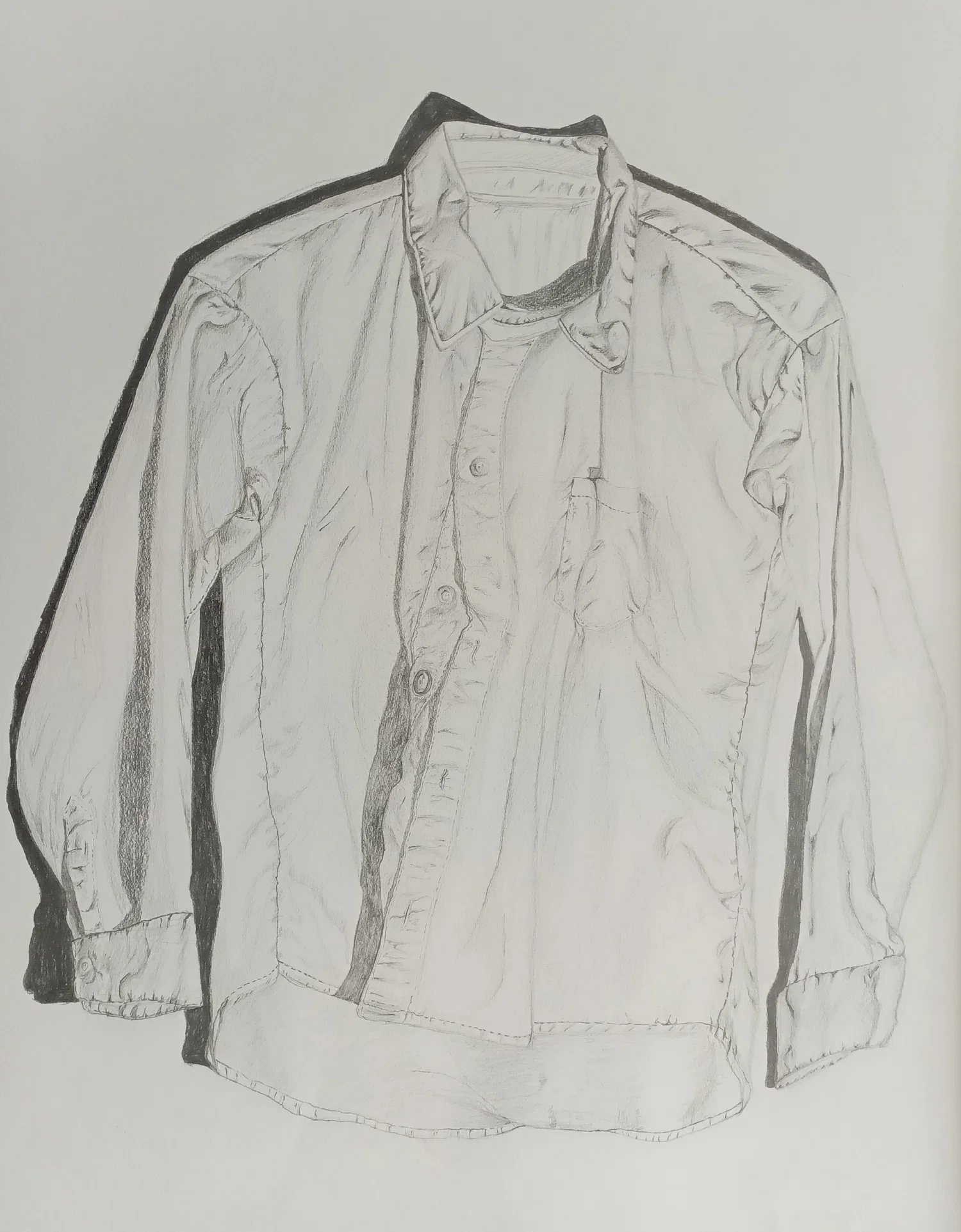 A pencil drawing of a long-sleeved button-up shirt hanging against a plain background. The shirt is slightly wrinkled, with visible folds along the sleeves, chest, and collar. Buttons run down the front, and a small pocket sits on one side of the chest. Soft shading and darker outlines emphasize the creases and the way the fabric drapes naturally.