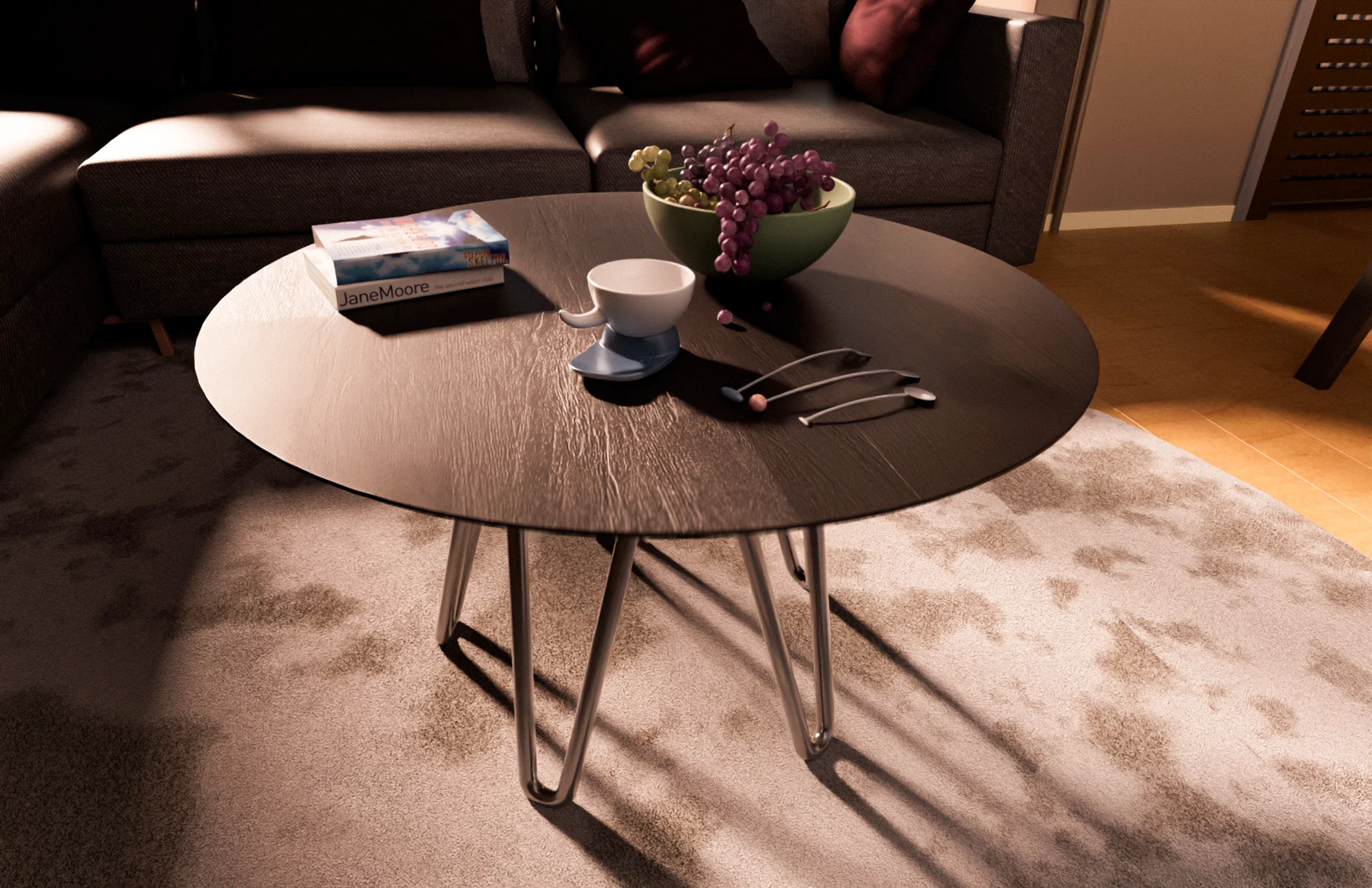 Alt Text A dark wood circular coffee table with silver hairpin legs sits on a textured rug in a sunlit living room. On the table, there is a bowl of purple grapes, a white teacup on a blue saucer, three decorative spoons, and two books stacked together. Soft afternoon light casts long shadows across the scene, with a grey sofa visible in the background.