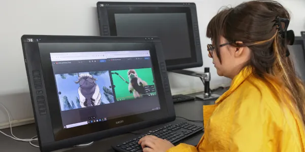 Female student wearing yellow sitting at a computer and working on a 3d design of an animated character