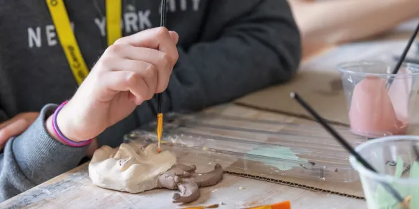 A Summer Youth Workshop student's hand paints a clay project