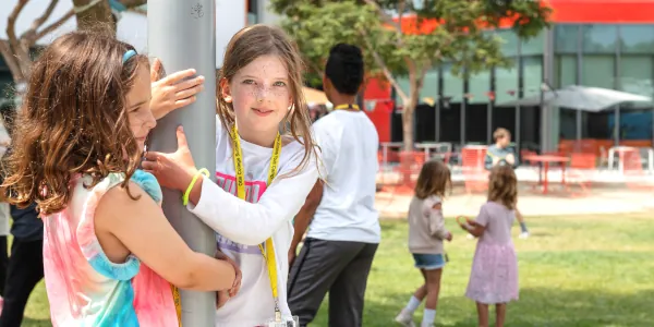Two female Summer Youth Camp students hugging a light pole