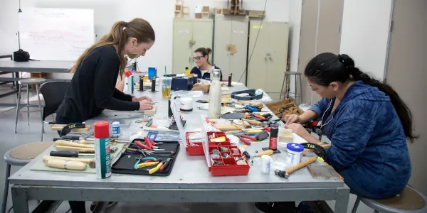 Three students at a long table with many jewelry making tools work on their projects