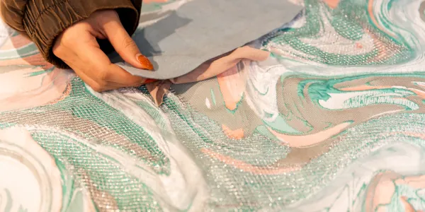 Female hand holding a swatch over fabric with a swirling durface design