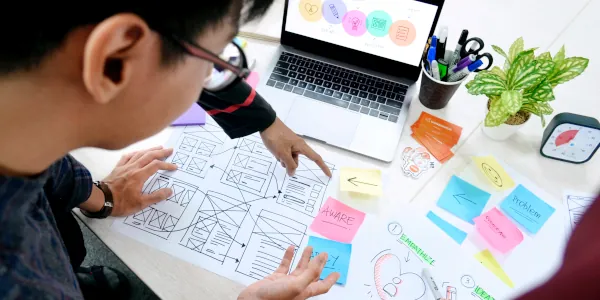 Two students with and a laptop work on a UX Design project