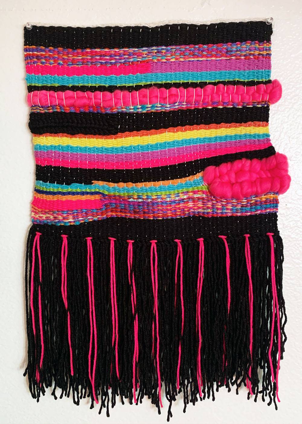 As part of my deliverables for my Senior Studio project, I created a weaving. This weaving was made on a loom with a variety of yarns, fibers, and ribbon. The final weaving is a tactile representation of my Mexican and American cultures and traditions being woven together to represent making connections. Weaving loom yarn design Mexican American 