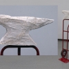 Mixed media in anvil form and mounted atop red moving dolly.