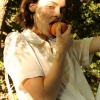 Woman licking a peach while gazing into the camera.