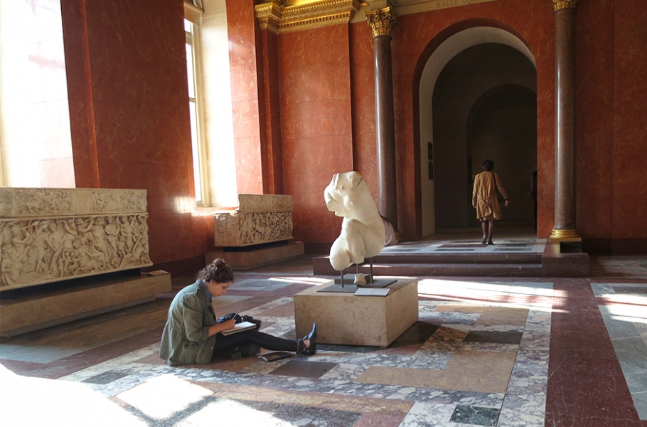 Art student sitting in a museum sketching a marble torso on