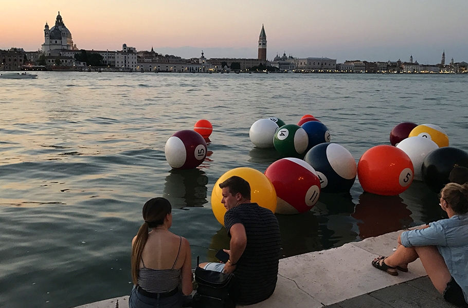 3 travel study students sit on a quay with large billiard ball shaped floats in the water