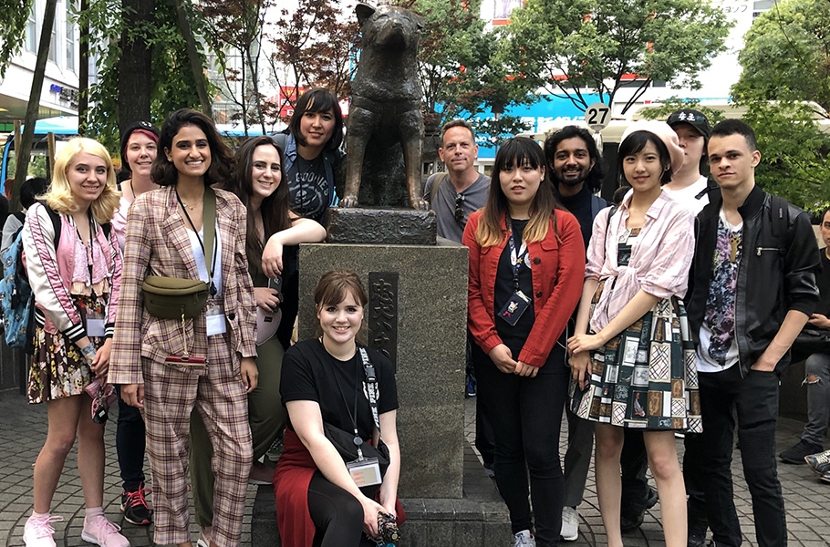 11 travel study students and their instructor gathered aroud the statue of a dog